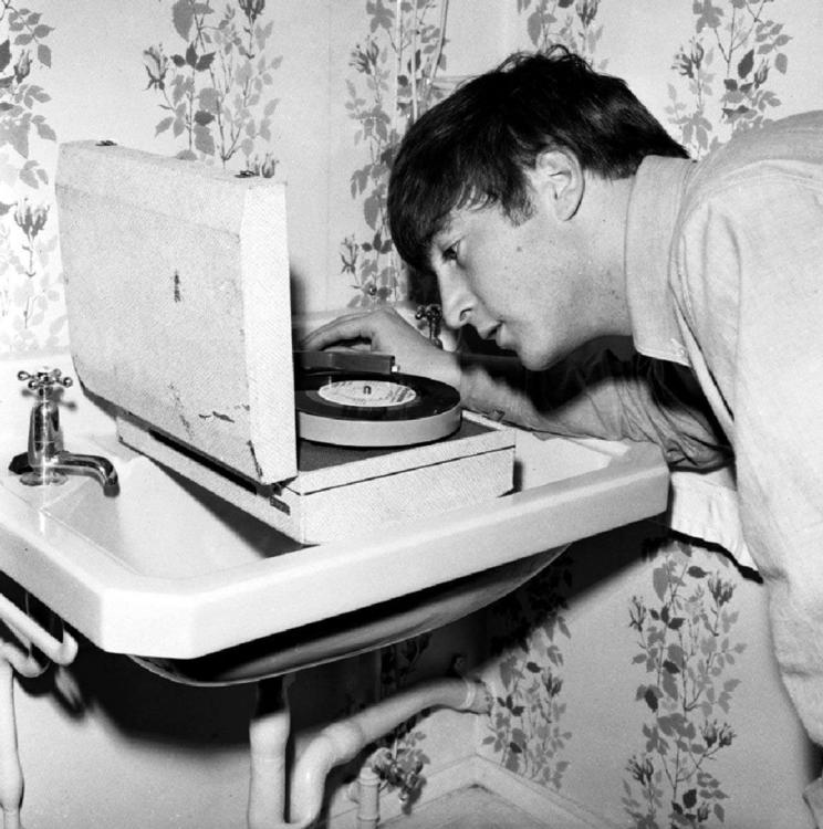 John Lennon (1940 - 1980) listening to a pre-release test pressing of the Twist And Shout EP on a portable record player that travelled with the group on tour here..jpg
